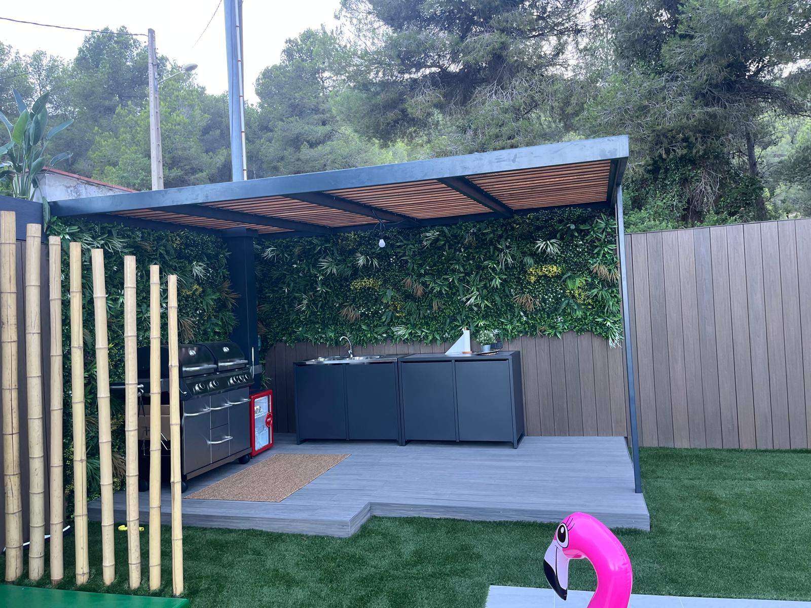 Cocina exterior y barbacoa bajo la pérgola con lamas de madera Diseño de jardín con piscina y césped en Sitges Cocina exterior y barbacoa bajo la pérgola con lamas de madera